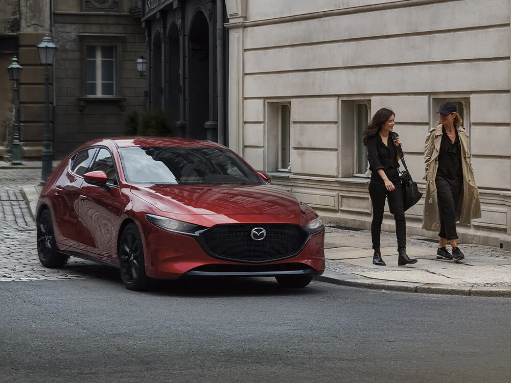 Red Mazda3 Sport driving past pedestrians in a historic district